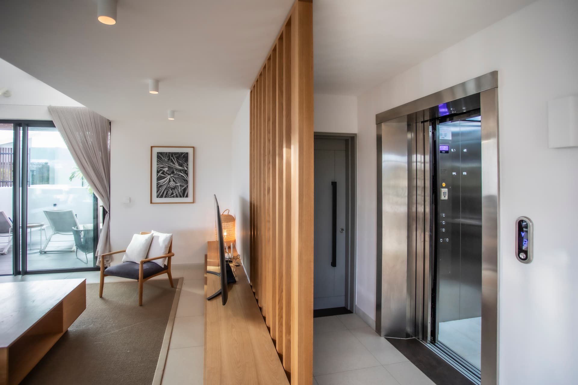 Galerie spacieuse avec éclairage intégré et circulation fluide entre les espaces.  
Mur en bois ajoutant une dimension chaleureuse à l'entrée.  
Accès direct à la terrasse depuis le séjour, favorisant la lumière naturelle.  
Éléments contemporains soulignant le design moderne de l'intérieur.  
Mobilier épuré et discret créant une atmosphère accueillante.