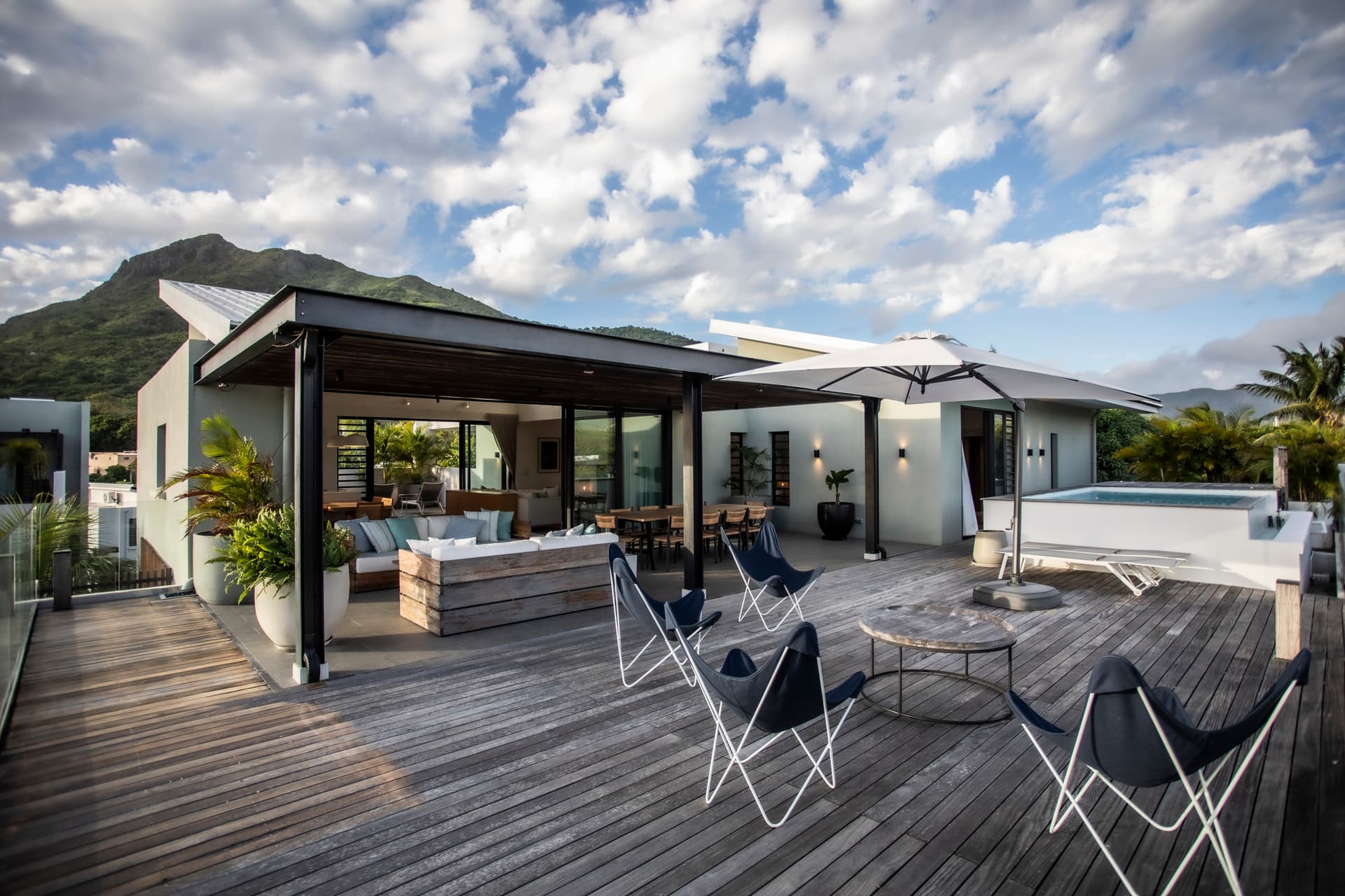 Galerie extérieure avec espace de vie confortable et vue sur la montagne. 

Mobilier en bois et sièges en toile favorisant une ambiance détendue. 

Parasols offrant de l'ombre pour se protéger du soleil. 

Terrasse en bois ajoutant un aspect chaleureux à l'environnement. 

Piscine privée visible, intégrant harmonieusement l'espace extérieur.