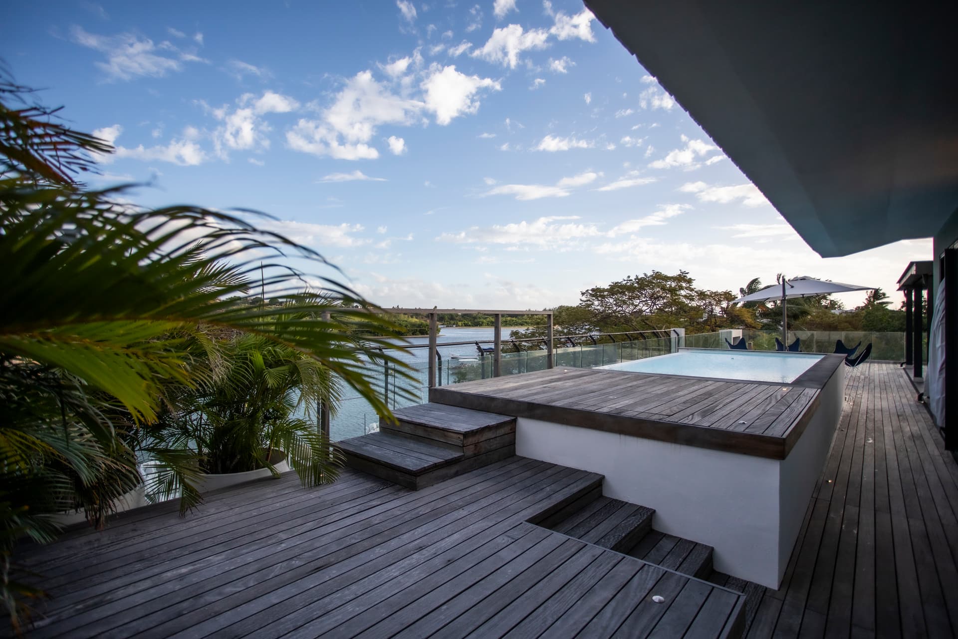 Terrasse en bois avec piscine privée offrant une vue sur la nature. 

Palmier ajoutant une touche tropicale à l'environnement extérieur. 

Zone de détente avec mobilier confortable pour profiter des journées ensoleillées. 

Escalier intégré facilitant l'accès à la piscine depuis l'espace. 

Éclairage extérieur permettant de prolonger les soirées en plein air.