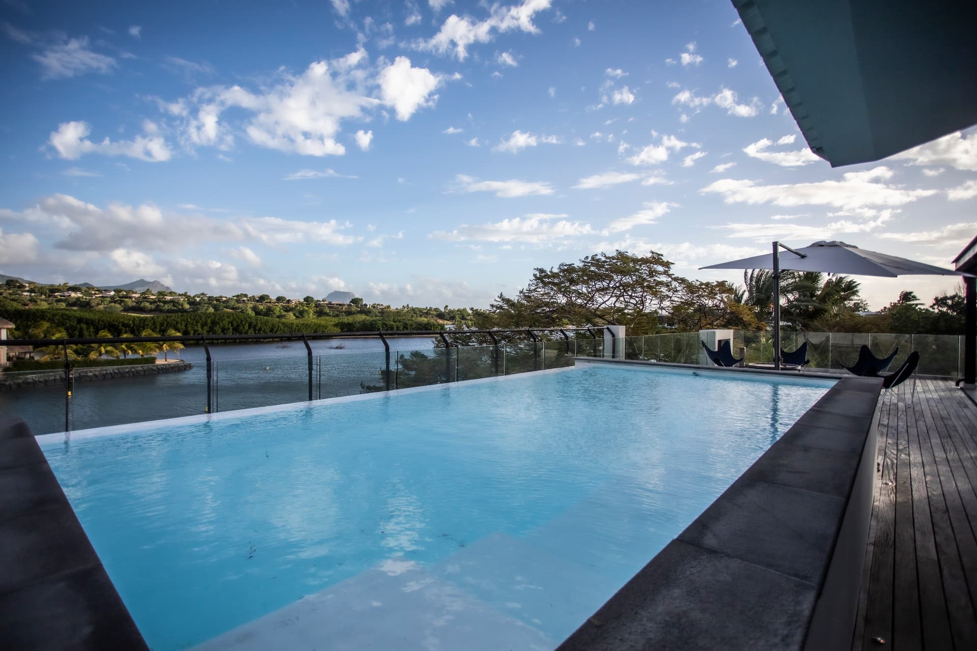 Terrasse avec piscine à débordement offrant une vue panoramique sur l'eau. 

Mobilier en bois disposé pour des moments de détente en extérieur. 

Parasols positionnés pour assurer de l'ombre au bord de la piscine. 

Espace de vie extérieur intégrant des chaises longues pour se relaxer. 

Éclairage extérieur créant une atmosphère agréable lors des soirées.