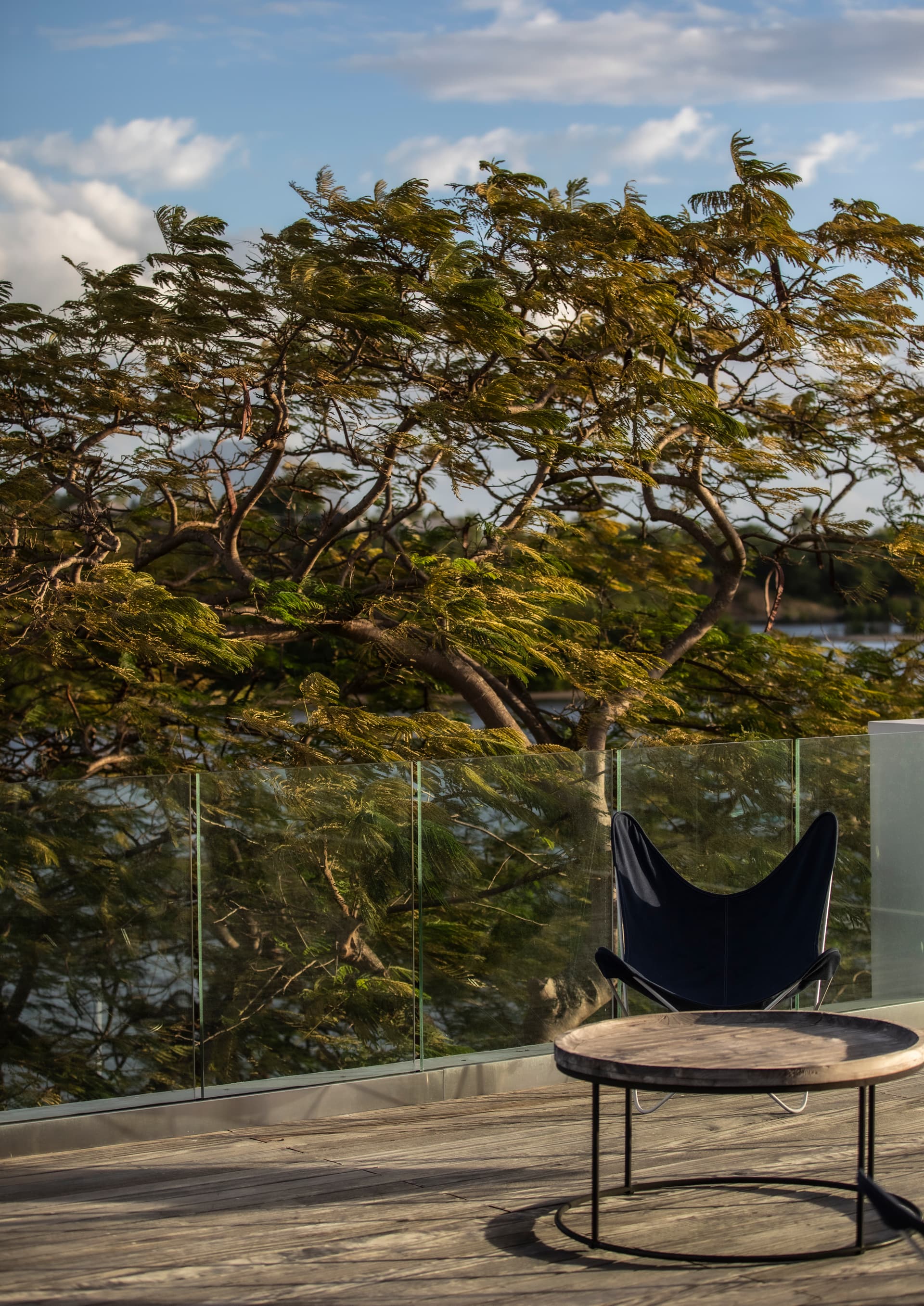 Espace extérieur avec fauteuil suspendu offrant une vue sur la nature. 

Terrasse en bois avec rambarde en verre pour une sécurité optimale. 

Mobilier moderne intégrant une table basse pour des moments conviviaux. 

Végétation environnante ajoutant une touche de verdure à l'espace. 

Chaises disposées pour profiter du paysage au bord de l'eau.