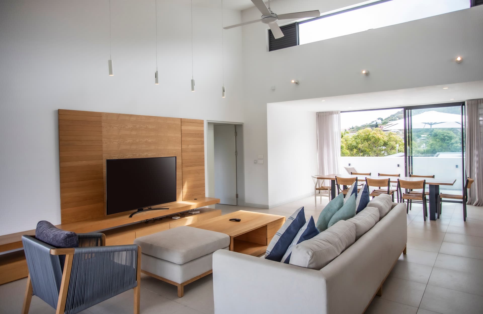 Espace de vie lumineux avec grandes fenêtres et décoration sobre.  
Canapé confortable face à un téléviseur pour des moments de détente.  
Table à manger en bois intégrée à l'espace pour les repas quotidiens.  
Plafond haut ajoutant une sensation d'espace et de luminosité.  
Accès direct à la terrasse depuis le salon pour profiter de l'extérieur.