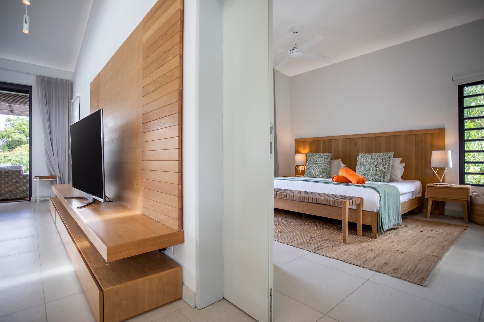 Chambre équipée d'un lit en bois et d'un espace de rangement pratique.  
Grandes fenêtres offrant une vue sur la nature environnante depuis l'intérieur.  
Coin salon adjacent avec accès direct à la terrasse extérieure.  
Mobilier minimaliste favorisant une ambiance apaisante et fonctionnelle.  
Tapis en fibres naturelles ajoutant une texture douce au sol.