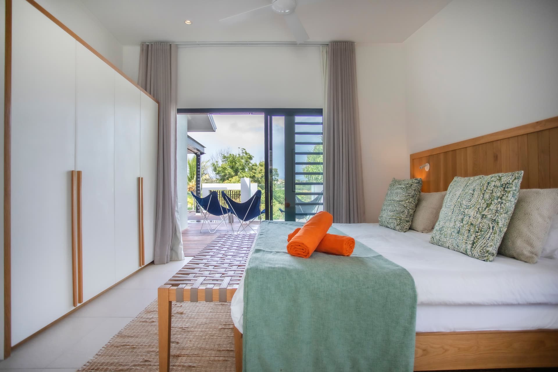 Chambre lumineuse avec accès direct à la terrasse extérieure.  
Lit avec têtes de lit en bois et déco minimaliste.  
Éléments naturels apportant une texture douce et apaisante.  
Fenêtres offrant une vue sur l'espace extérieur et la végétation.  
Mobilier fonctionnel intégrant un espace de rangement pratique.