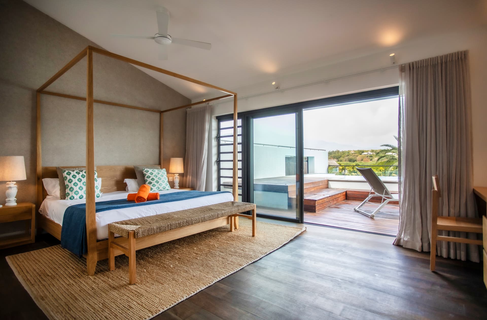 Chambre avec accès direct à une terrasse en bois.  
Lit à baldaquin ajoutant une touche de confort.  
Grandes fenêtres offrant une vue sur l'extérieur.  
Mobilier en bois clair pour une atmosphère apaisante.  
Tapis en jute apportant une texture naturelle à l'espace.