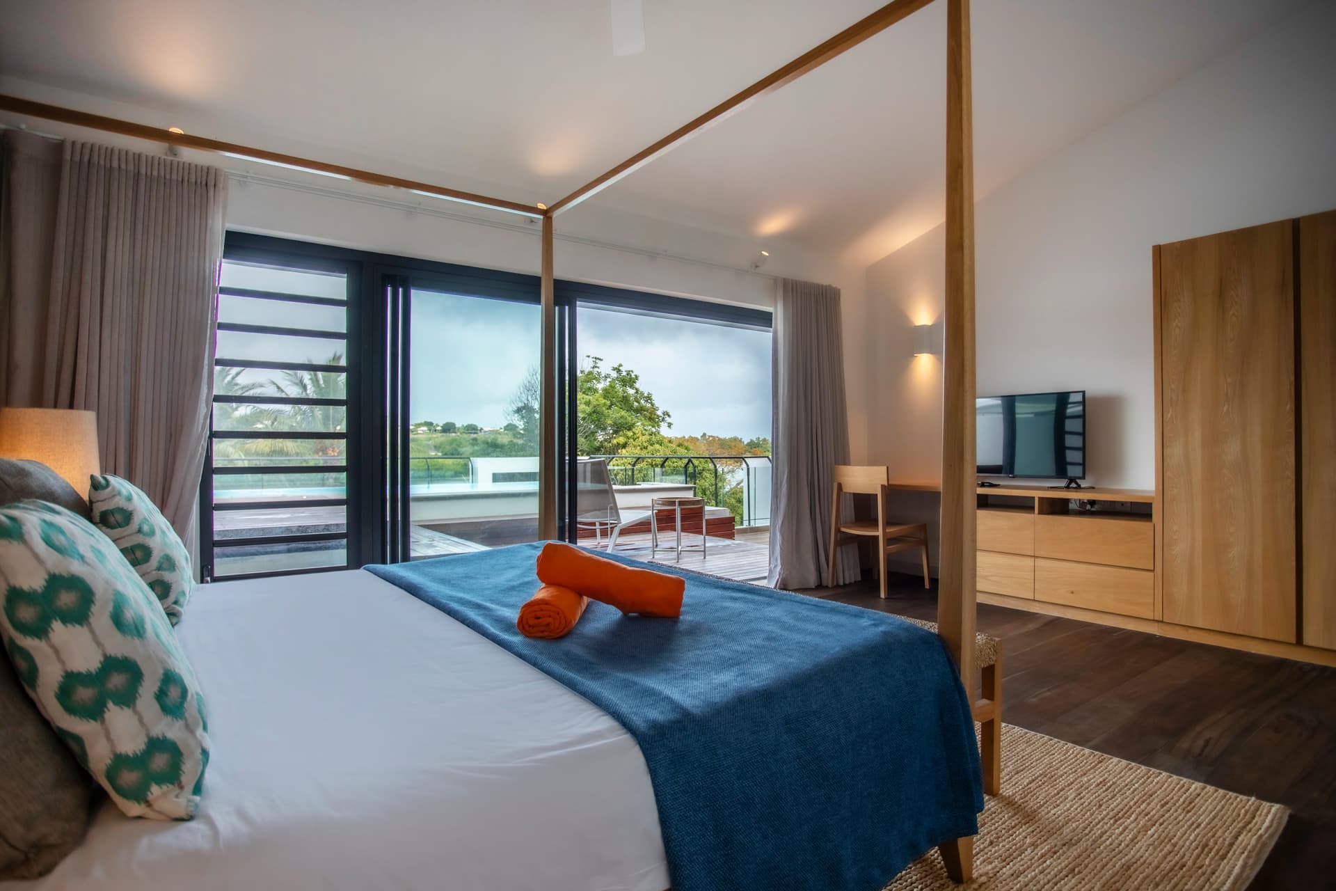Chambre avec lit à baldaquin et accès à la terrasse en bois.  
Baies vitrées offrant une vue sur la piscine privée.  
Mobilier en bois clair ajoutant de la simplicité à l'espace.  
Tapis texturé apportant une touche de confort sous les pieds.  
Espace de rangement intégré pour une meilleure organisation.