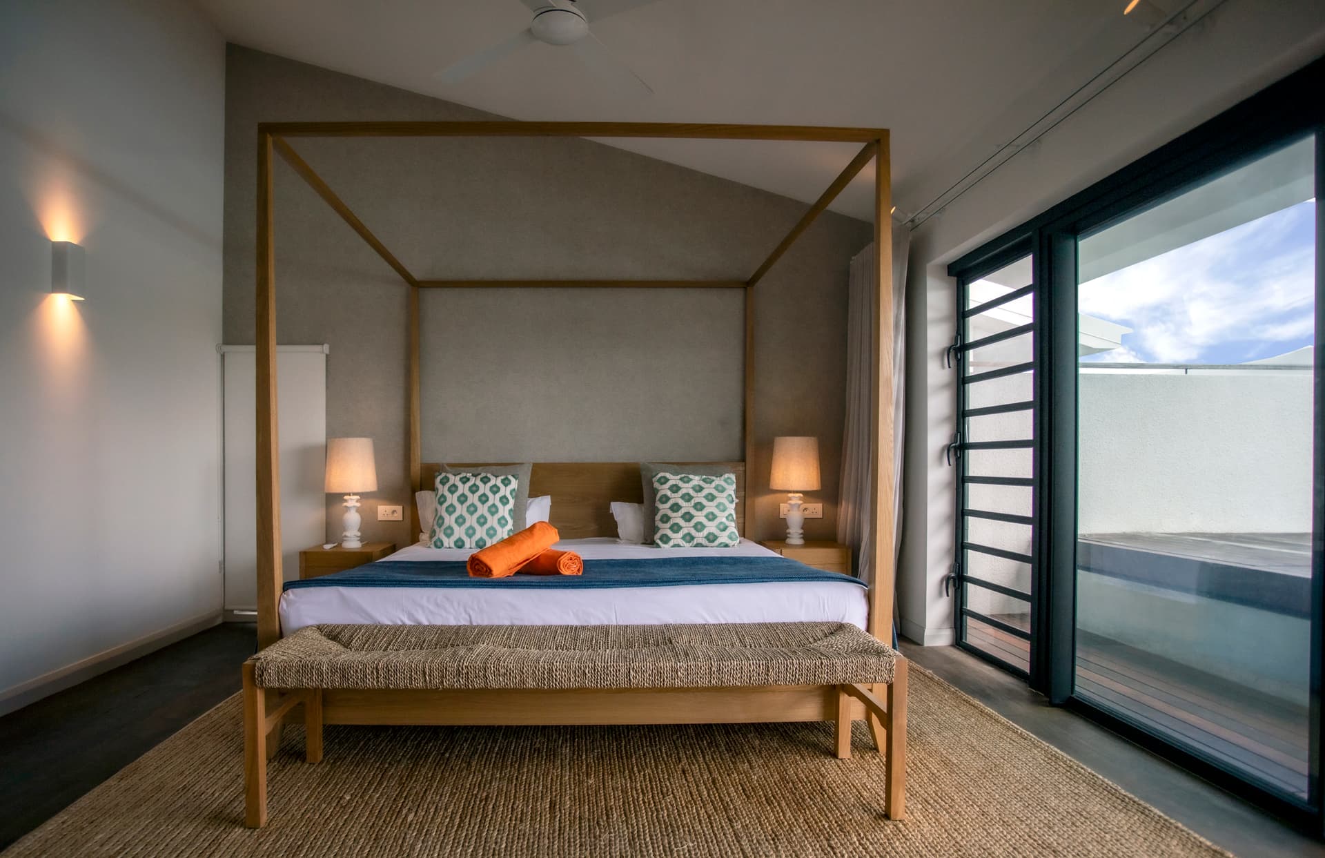 Chambre spacieuse avec un lit à baldaquin et accès à une terrasse.  
Luminaires encastrés apportant une luminosité adaptée à l'espace.  
Fenêtres panoramiques offrant une vue dégagée sur l'extérieur.  
Mobilier en bois clair créant une atmosphère tranquille.  
Tapis texturé ajoutant confort et chaleur au sol.