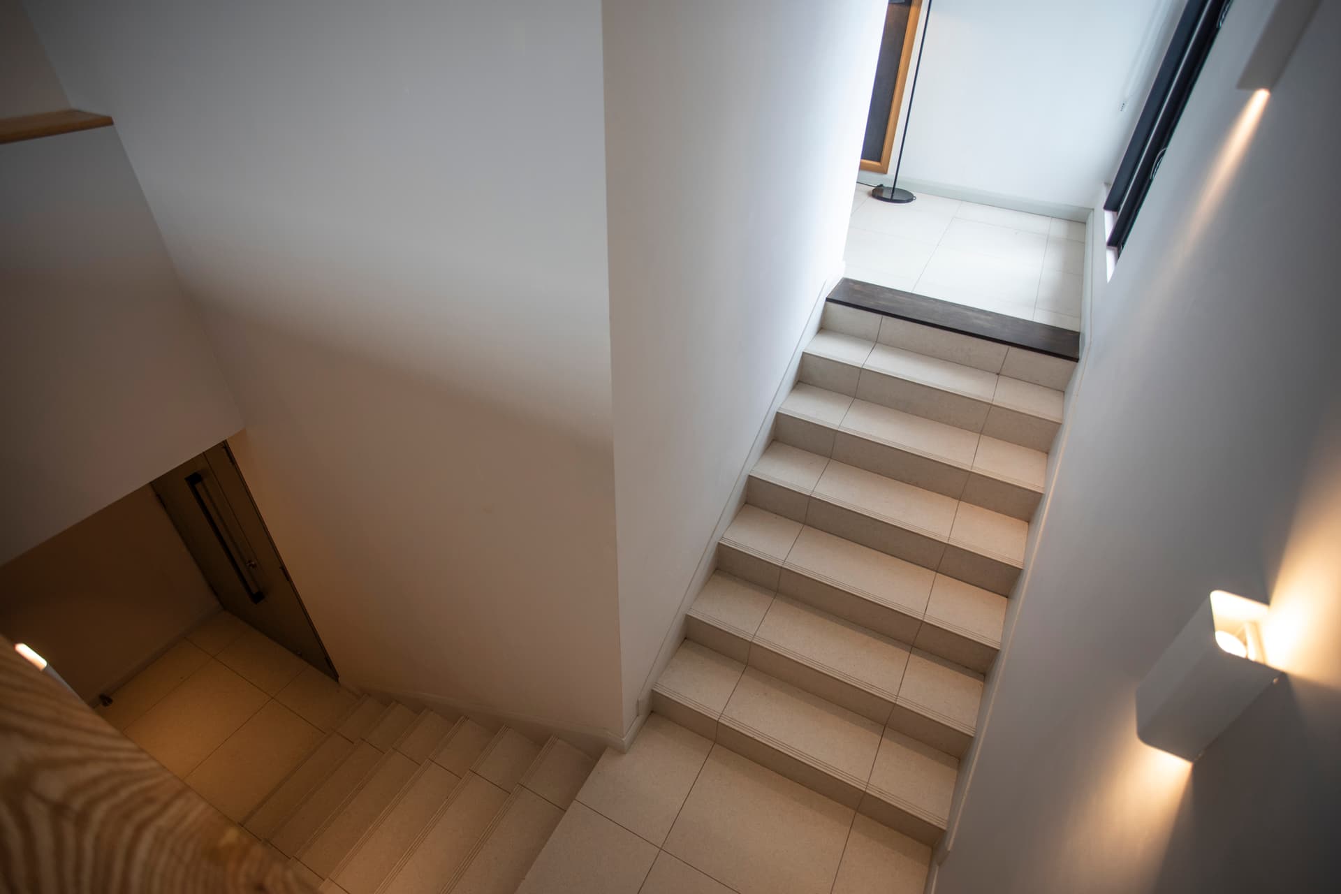 Escalier menant aux différents niveaux du penthouse.  
Murs blancs et lumière naturelle offrant une atmosphère ouverte.  
Marches carrelées facilitant la circulation entre les espaces.  
Éclairage intégré mettant en valeur la structure de l'escalier.  
Vue dégagée sur le reste du penthouse depuis le haut.