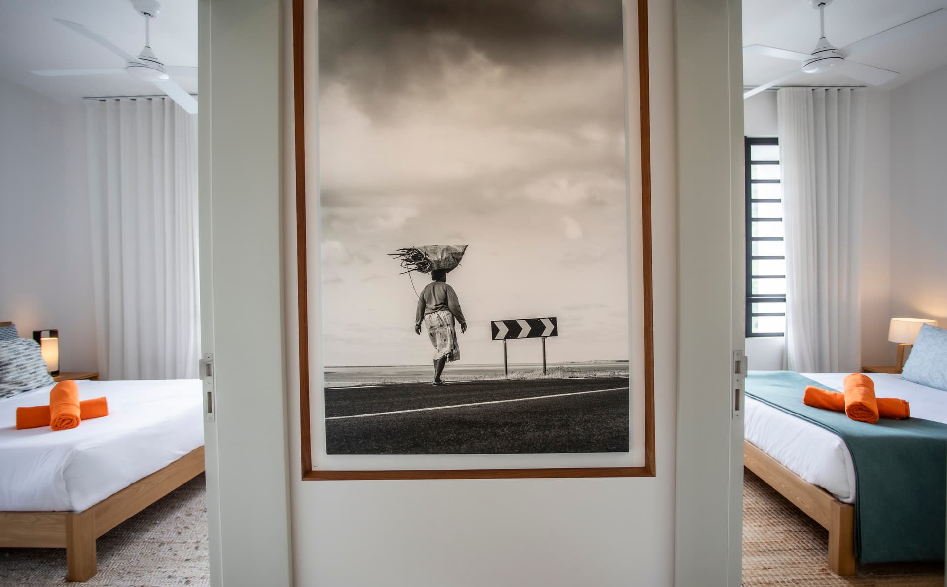 Photographie en noir et blanc encadrée créant un point focal dans l'espace.  
Sol en jute ajoutant une texture naturelle au couloir.  
Lits jumeaux avec linge de lit coordonné pour un style harmonieux.  
Éclairage doux sur les murs blancs pour une atmosphère apaisante.  
Rideaux occultants assurant intimité et obscurité dans