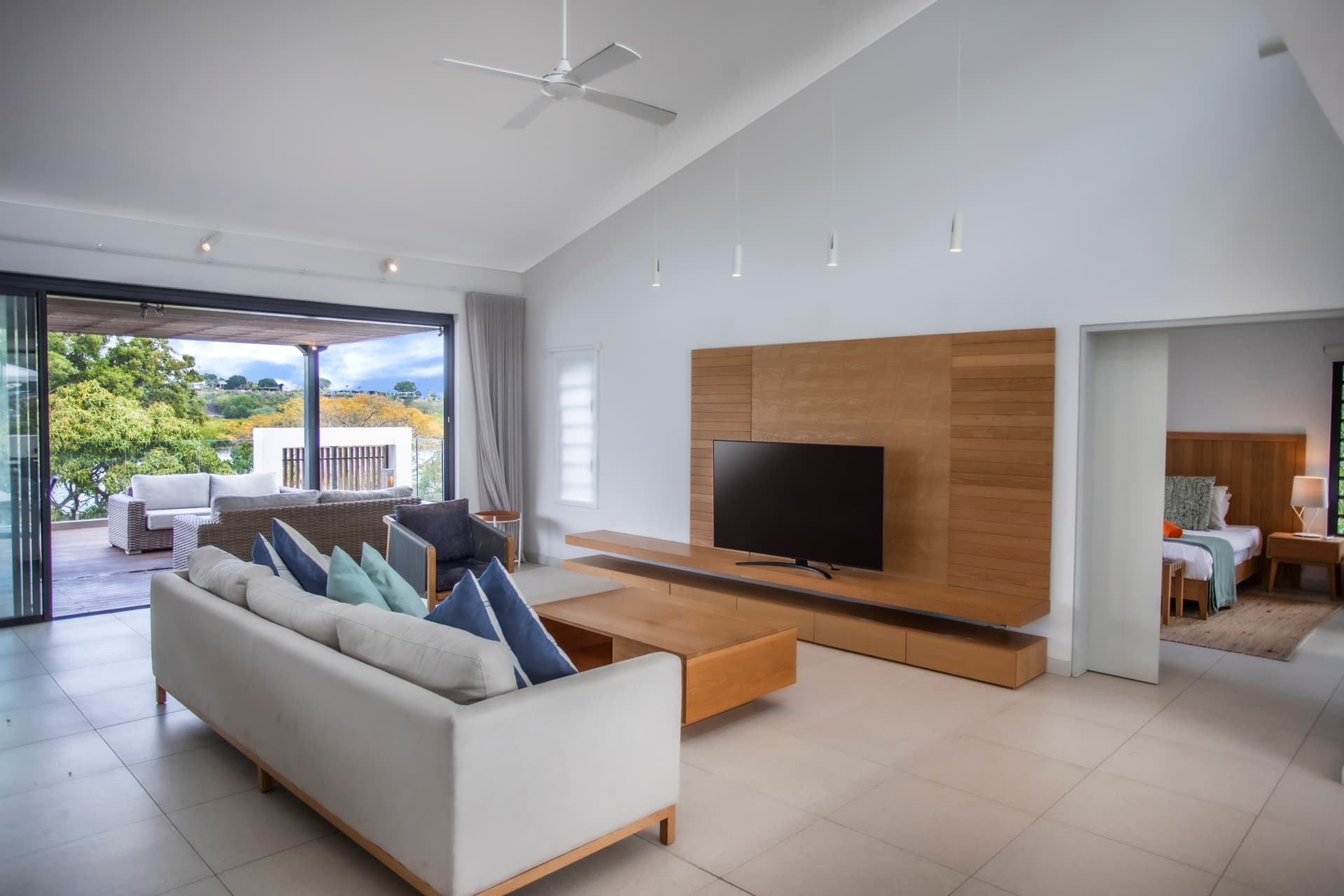 Espace de vie spacieux avec lumière naturelle et vue sur l'extérieur.  
Canapé moderne et table basse en bois créent un environnement fonctionnel.  
Télévision murale intégrée pour un divertissement accessible.  
Accès direct à la terrasse, prolongeant l'espace de vie.  
Ventilateur de plafond ajoutant confort et circulation d'air.