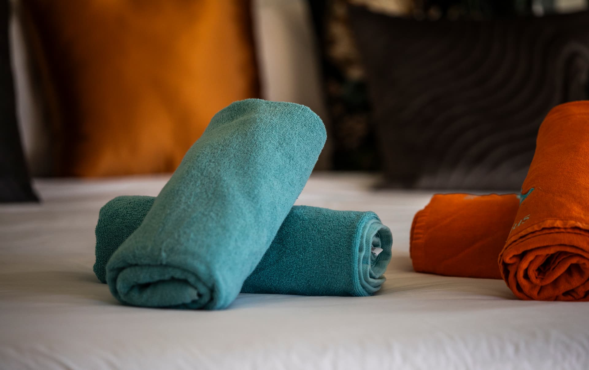 Galerie avec serviettes de bain bien pliées sur le lit. Couleurs vives et détails texturés.