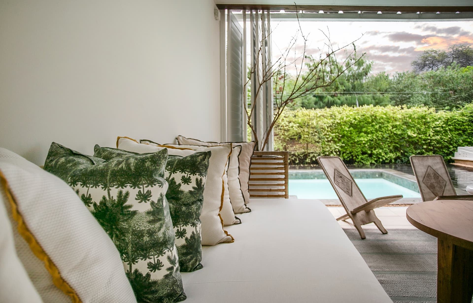 Tons verts des coussins apportent une touche naturelle à l'espace.  
Mobilier en bois clair créant un coin détente près de la piscine.  
Végétation environnante renforce l'intimité tout en embellissant l'espace.  
Lumière douce filtrant à travers les fenêtres, ajoutant une ambiance sereine.  
Sol en textile tissé offrant confort et chaleur à l