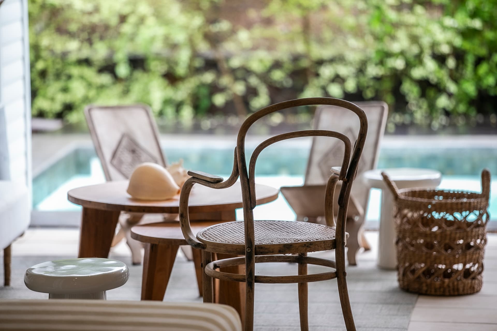 Espace de détente extérieur avec chaises en bois et tables. Vue sur la piscine adjacente. Végétation environnante offrant intimité et fraîcheur. Mobilier simple pour des moments de relaxation. Ambiance calme avec lumière naturelle.