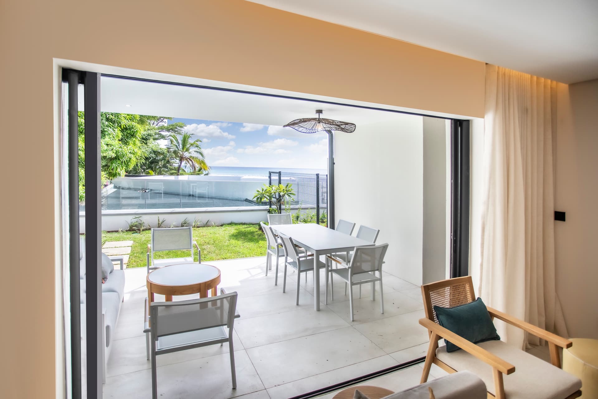 Tons clairs dominants dans l'espace de vie ouvert sur l'extérieur.  

Salle à manger lumineuse avec accès direct à la terrasse.  

Mobilier moderne complétant l'agencement intérieur minimaliste.  

Vues sur la verdure et la mer depuis les grandes baies vitrées.  

Espace de vie conçu pour maximiser la lumière naturelle.  

Terrasse bien intégrée
