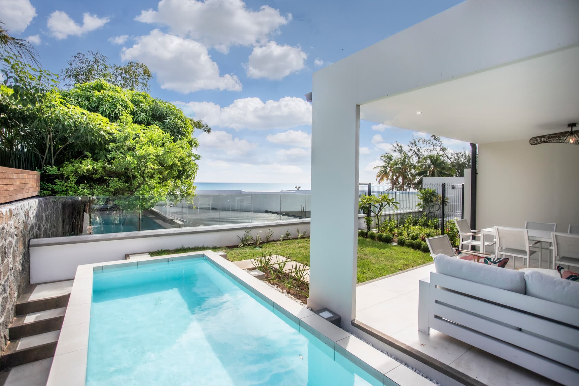 Espace extérieur avec piscine donnant sur un jardin bien agencé.  
Terrasse ouverte offrant une vue dégagée sur l'océan.  
Mobilier moderne disposé pour des moments de détente au bord de l'eau.  
Végétation soigneusement plantée ajoutant de la fraîcheur à l'environnement.  
Accès direct à la piscine depuis le salon lumineux.  
Lumière naturelle abond