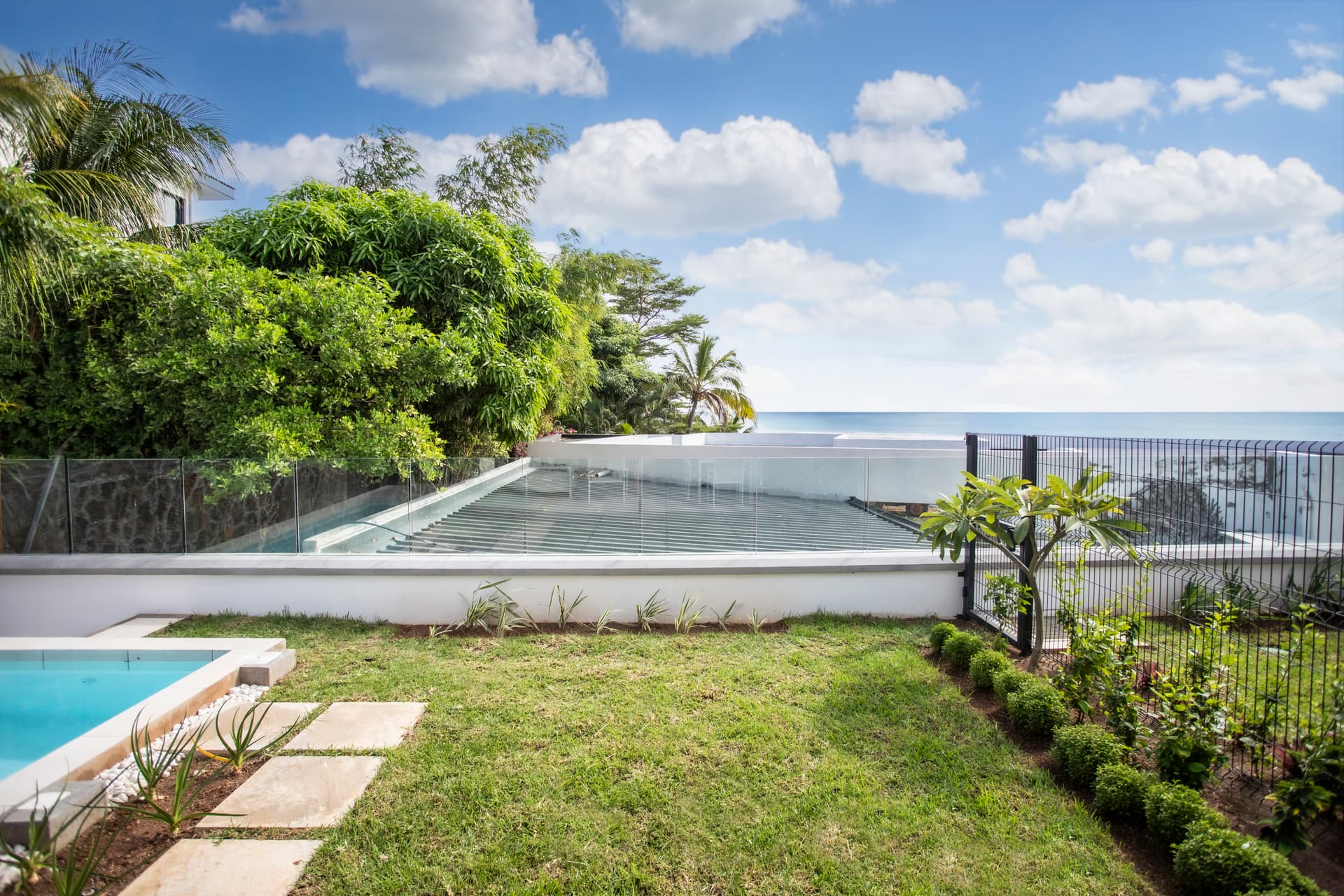 Espace extérieur avec piscine à débordement offrant une vue sur l'océan.  
Jardin bien entretenu entourant la piscine et l'espace de vie.  
Terrasse ouverte dotée de mobilier pour profiter de l'environnement.  
Végétation tropicale apportant une touche de fraîcheur et de verdure.  
Lumière naturelle abondante grâce aux grandes baies vitrées.