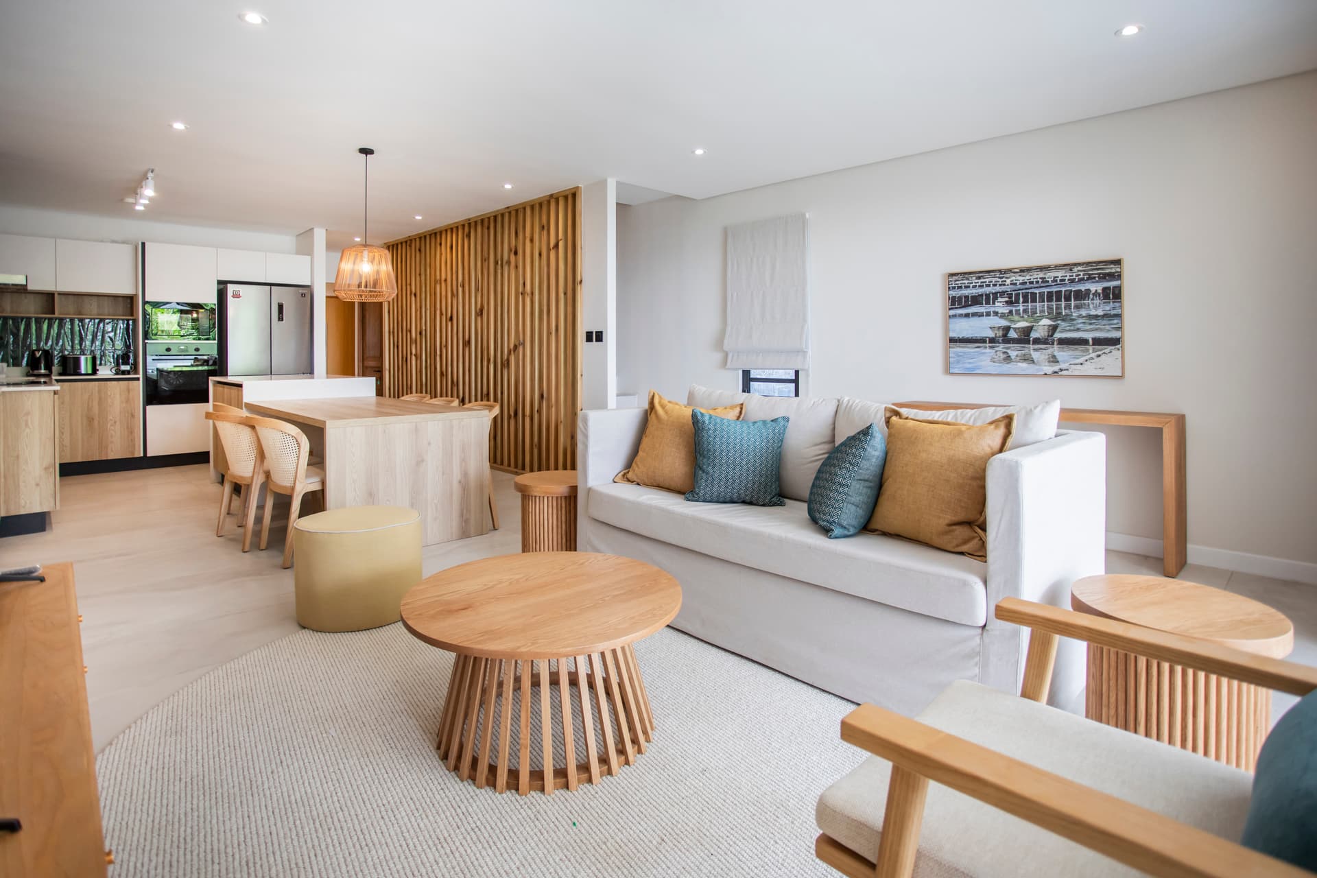 Espace salon avec mobilier en bois et textile doux.  
Baies vitrées laissant entrer beaucoup de lumière naturelle.  
Coin repas intégré offrant une vue sur l'extérieur.  
Mobilier contemporain disposé harmonieusement pour un confort optimal.  
Sol en matériaux clairs, apportant une ambiance lumineuse.