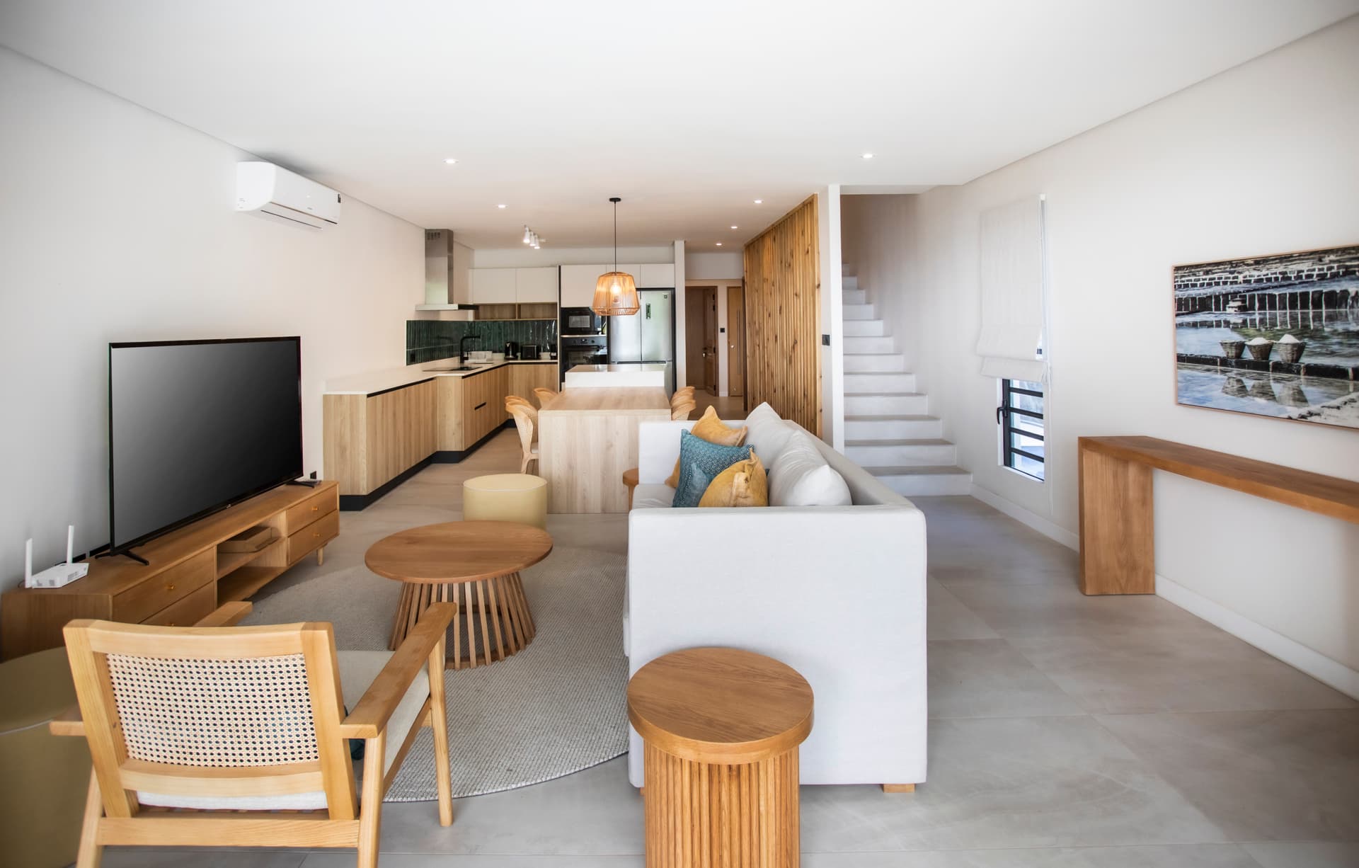 Espace salon lumineux avec mobilier en bois et textile doux.  
Baies vitrées offrant une vue sur l'extérieur verdoyant.  
Coin repas intégré dans un agencement contemporain et ouvert.  
Lumière naturelle inondant la pièce grâce à de larges ouvertures.  
Mobilier épuré créant une atmosphère moderne et fonctionnelle.