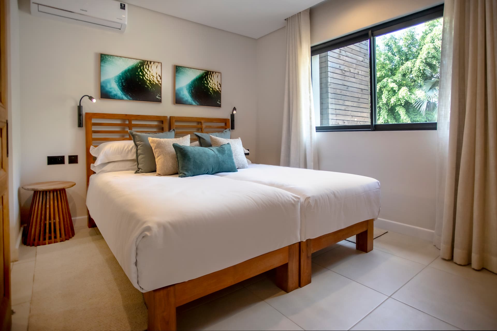 Chambre lumineuse avec un lit double et vue sur l'extérieur.  
Décoration simple avec œuvres d'art murales et coussins colorés.  
Éclairage naturel grâce à une grande fenêtre à proximité.  
Mobilier en bois ajoutant une note chaleureuse à l'espace.  
Tapis clair apportant une touche de confort au sol.