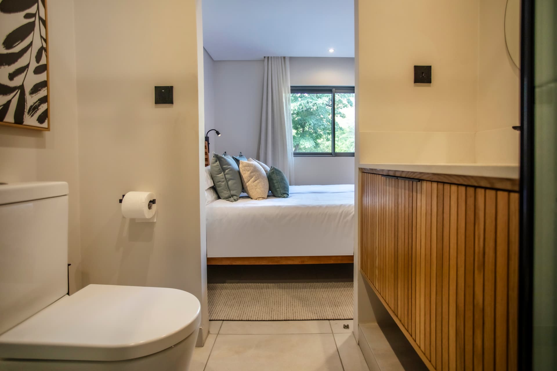 Salle de bain avec douche à l'italienne et meuble en bois.  
Miroir positionné au-dessus du plan de lavabo pour une utilisation pratique.  
Éclairage intégré assurant une luminosité adéquate pour les soins quotidiens.  
Toilette séparée offrant un espace fonctionnel et discret.  
Décoration minimaliste avec des couleurs neutres créant une ambiance calme.