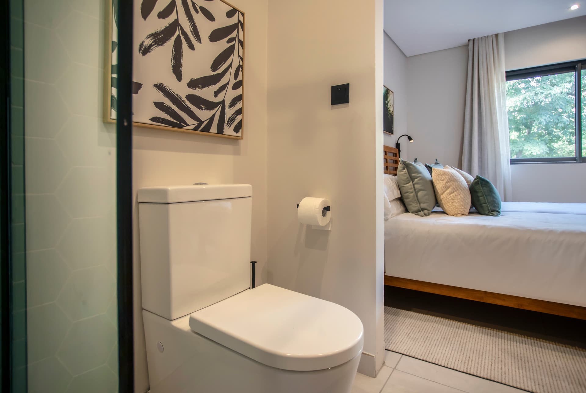 Toilette avec un design fonctionnel et un mur décoratif sobre.  
Espace optimisé avec un éclairage naturel provenant de la fenêtre.  
Mobilier en bois ajoutant une touche de chaleur à l'ensemble.  
Sols en carrelage clair offrant une facilité d'entretien.  
Vue sur l'extérieur grâce à une fenêtre bien positionnée.