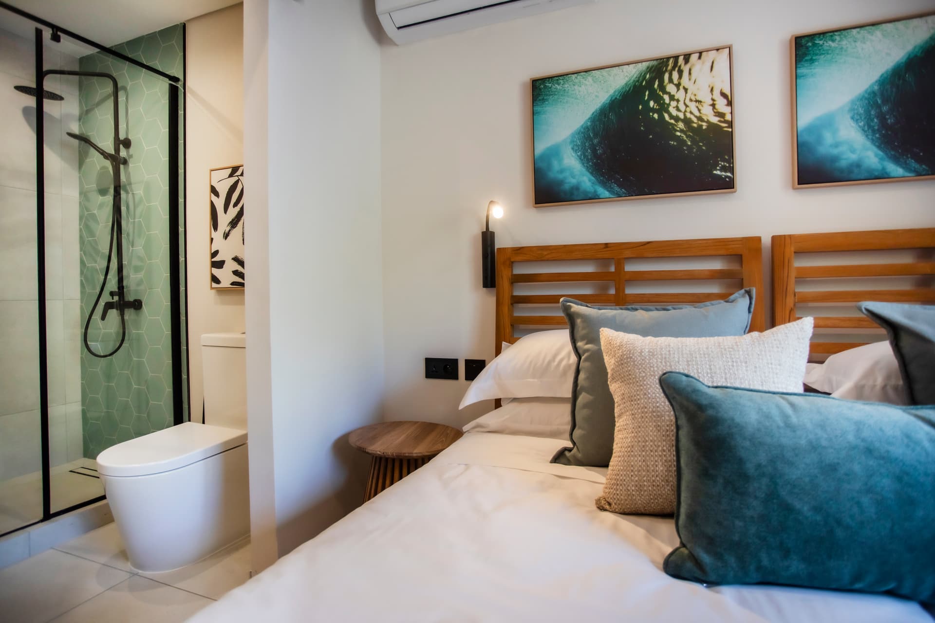 Chambre avec lit double et décor sobre, offrant une vue sur l'extérieur.  
Salle de bain attenante avec douche à l'italienne et carrelage clair.  
Éclairage moderne et appliques murales créant une ambiance chaleureuse.  
Coussins en velours ajoutant une touche de confort sur le lit.  
Mobilier en bois intégrant des éléments pratiques et est