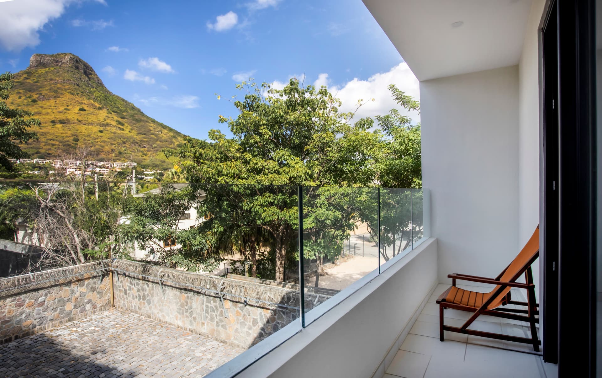 Balcon avec vue dégagée sur la verdure environnante.  
Chaise longue en bois offrant un espace de détente extérieur.  
Paroi en verre garantissant une vue panoramique sans obstruction.  
Environnement calme propice à la relaxation en plein air.  
Éléments naturels environnants ajoutant une touche de sérénité.
