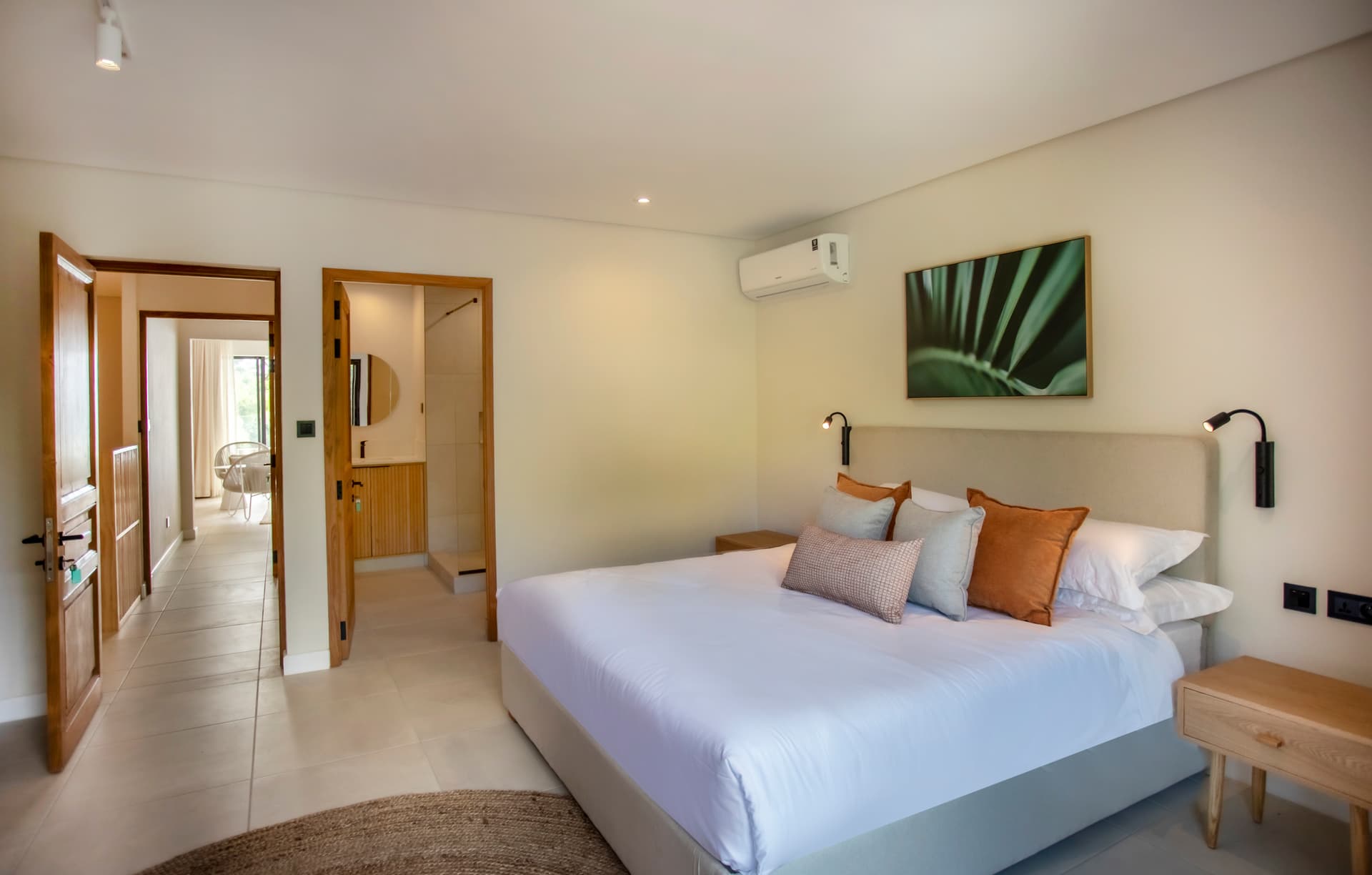 Chambre spacieuse avec lit double et éclairage intégré.  
Mobilier en bois clair ajoutant une touche moderne à l'ensemble.  
Sols en carrelage clair pour un entretien facile et pratique.  
Accès direct à une salle de bain attenante avec douche.  
Fenêtre offrant une vue sur l'extérieur et une lumière naturelle.