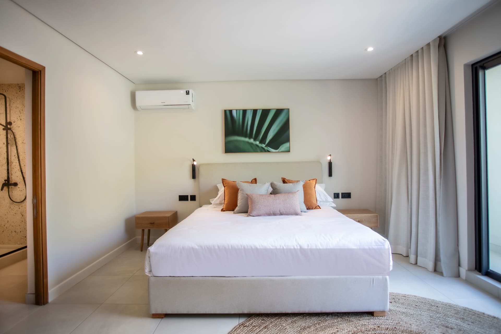Chambre lumineuse avec lit double et éclairage intégré moderne.  
Tapis en jute ajoutant une texture naturelle au sol.  
Mobilier en bois clair offrant un espace de rangement pratique.  
Fenêtre laissant entrer la lumière naturelle et vue dégagée.  
Salle de bain attenante avec douche à l'italienne et carrelage clair.