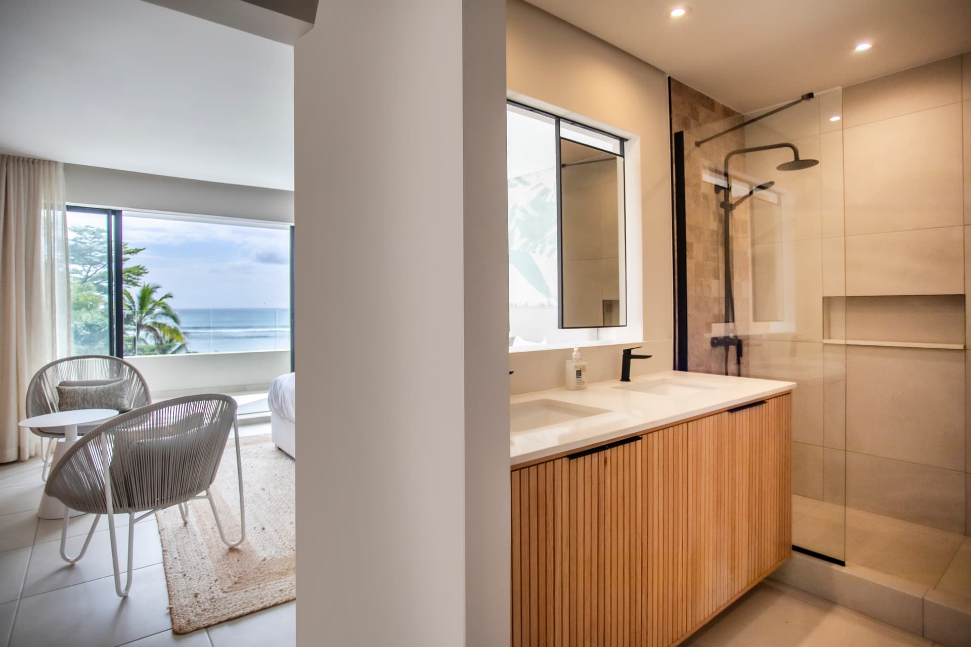 Textures claires et naturelles dans cette salle de bain moderne.  
Douche à l'italienne avec paroi en verre optimisant l'espace.  
Éclairage intégré offrant une luminosité agréable dans la pièce.  
Mobilier en bois clair pour un rangement pratique et esthétique.  
Fenêtre laissant entrer la lumière naturelle et vue sur l'extérieur.