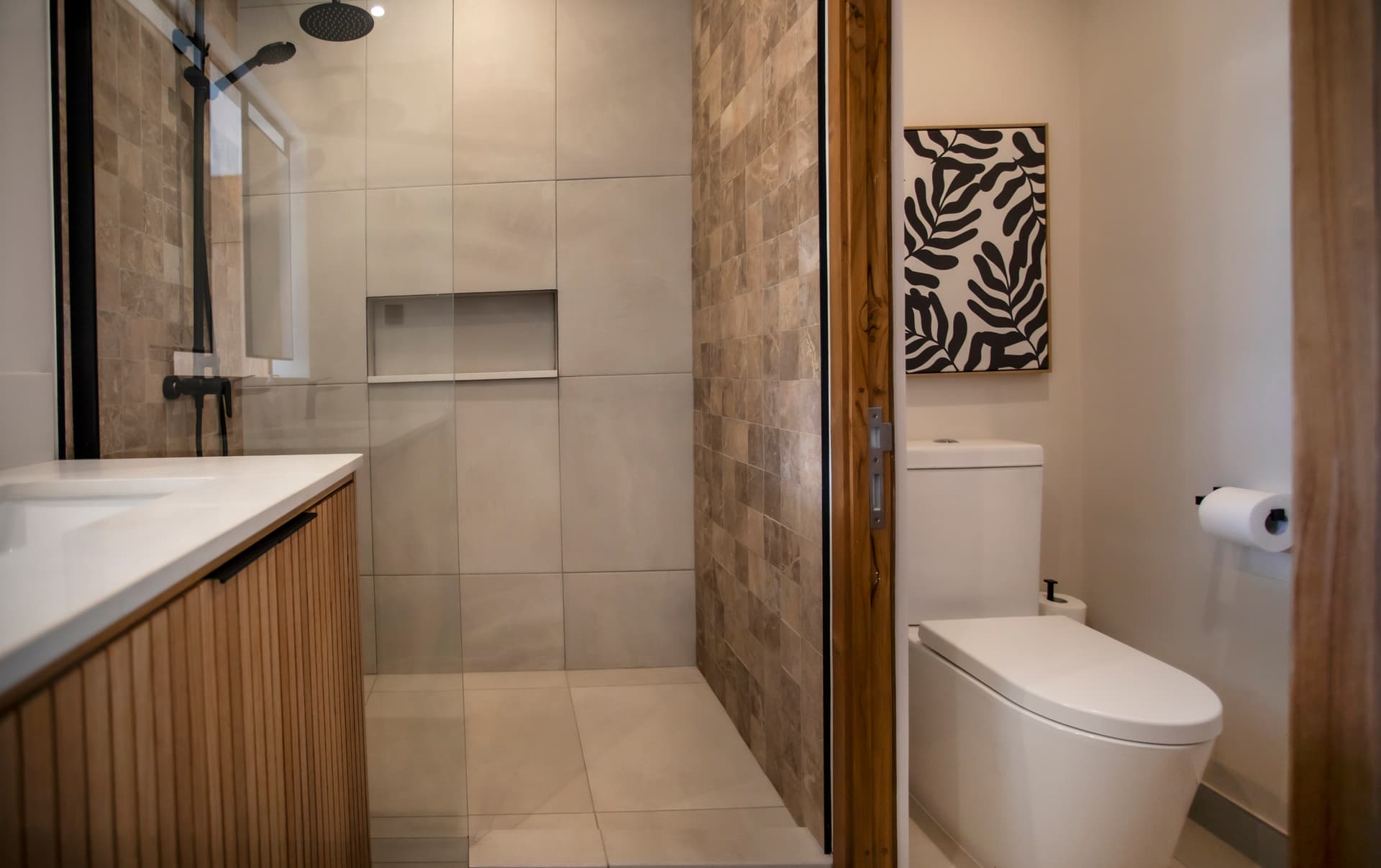 Revêtement en pierre texturé dans cette douche à l'italienne spacieuse.  
Mobilier en bois clair offrant un rangement fonctionnel sous le lavabo.  
Éclairage intégré assurant une luminosité agréable et uniforme.  
Miroir élégant au-dessus du lavabo pour un aspect contemporain.  
Fenêtre laissant entrer la lumière naturelle, optimisant l'espace.