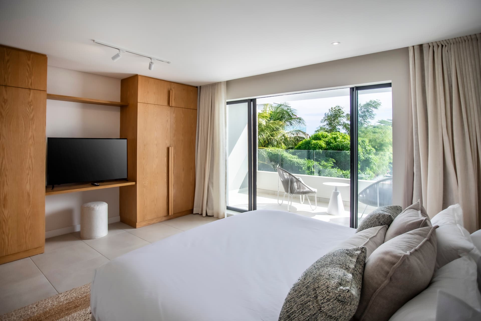 Tons clairs et linéaires dans une chambre avec accès à un balcon.  
Baies vitrées offrant une vue apaisante sur la verdure environnante.  
Mobilier en bois clair et moderne intégrant des rangements pratiques.  
Éclairage intégré créant une ambiance chaleureuse et lumineuse.  
Rangement discret et fonctionnel maximisant l'espace disponible.