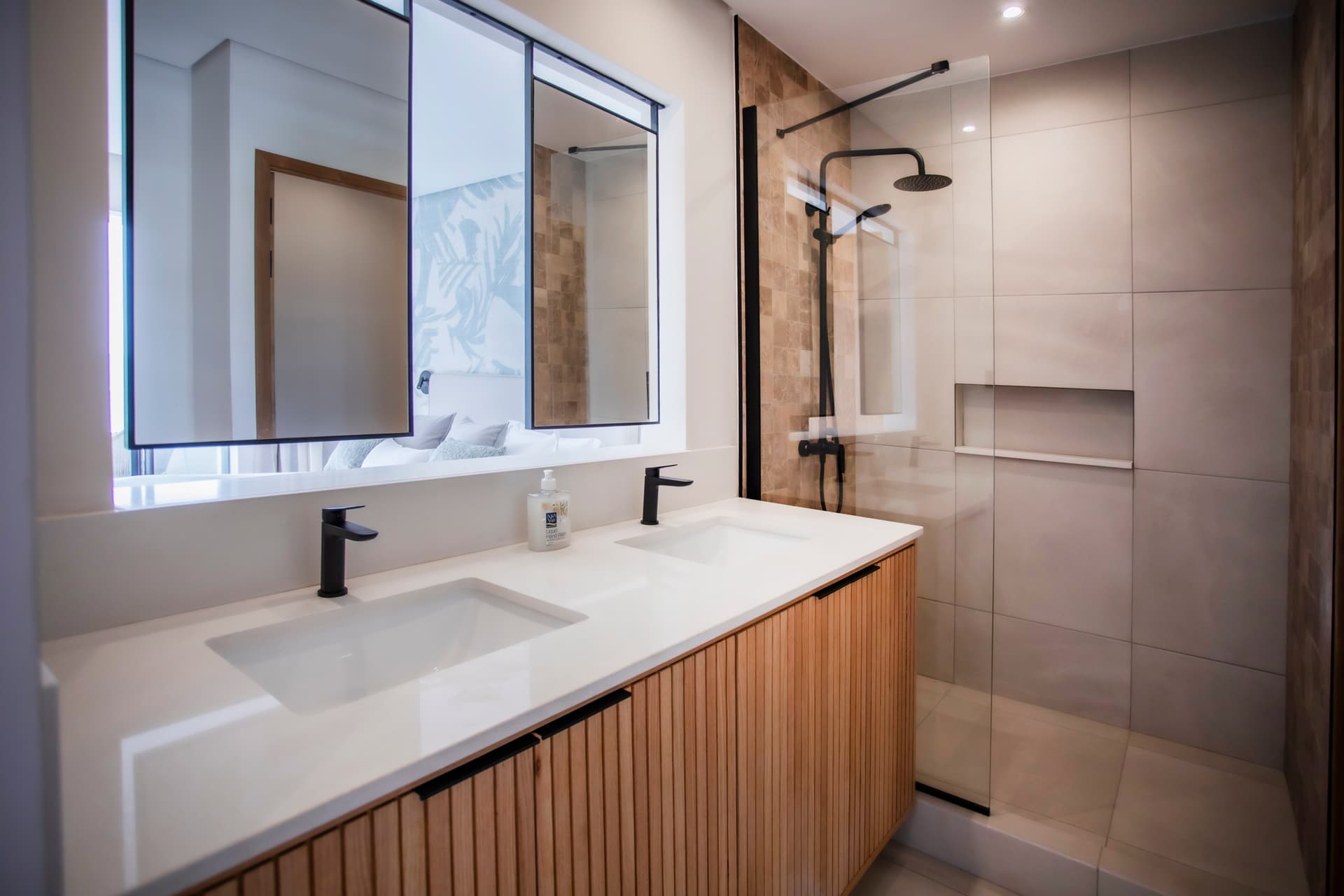 Salle de bains avec double vasque et meubles en bois clair.  
Douche à l'italienne avec parois en verre pour un accès pratique.  
Éclairage moderne et miroir large offrant une bonne luminosité.  
Sol carrelé facile d'entretien et esthétique pour un usage quotidien.  
Détails soigneusement intégrés pour une fonctionnalité optimale.