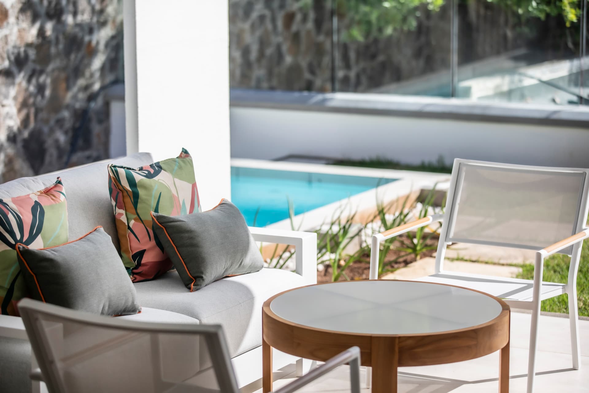 Espace extérieur avec salon moderne et coussins colorés.  
Vue sur la piscine depuis l'espace de détente.  
Mobilier en rotin offrant confort et style au balcon.  
Terrasse ensoleillée adjacente à la piscine pour se relaxer.  
Détail floral sur les coussins ajoutant une touche de couleur.