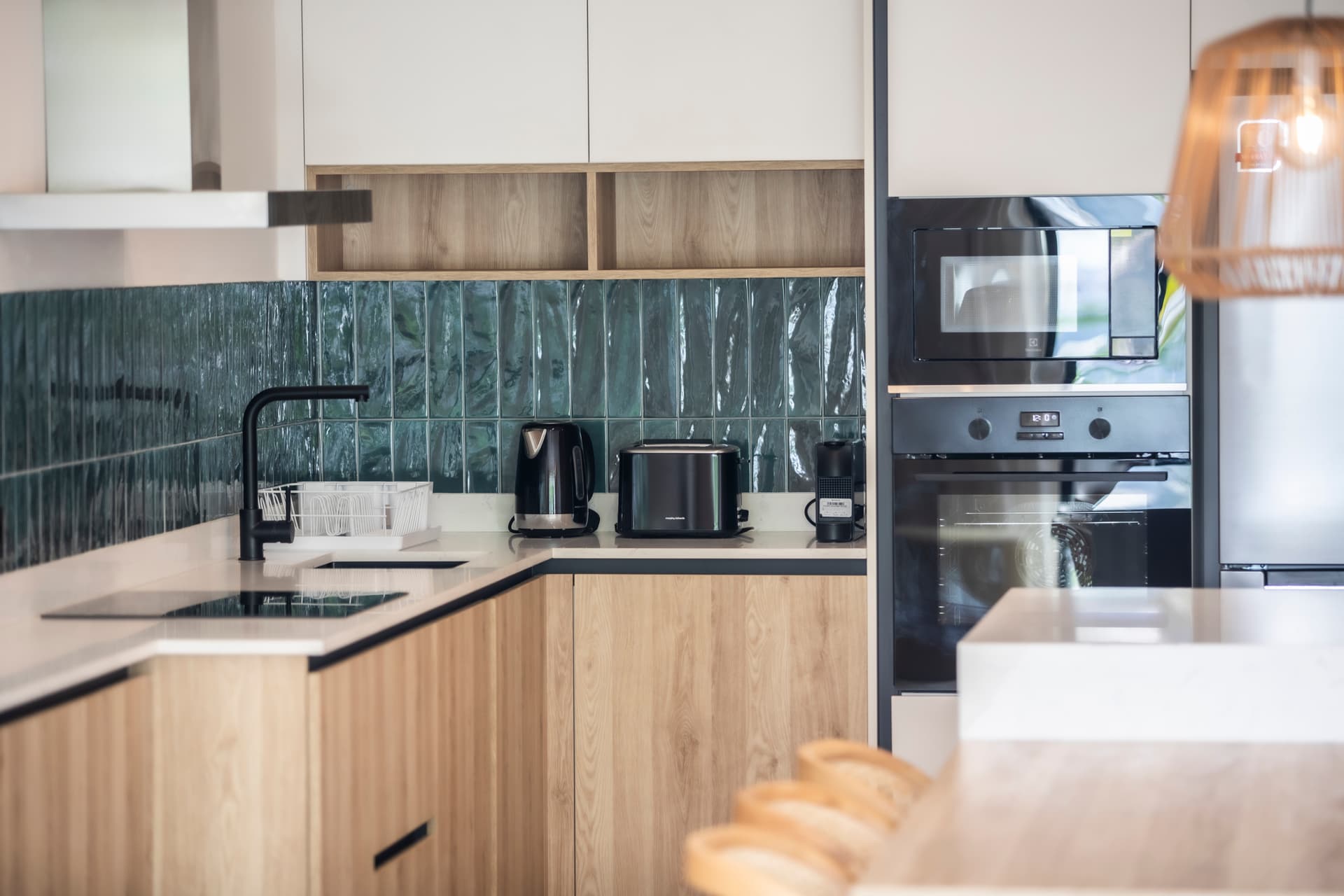 Cuisine équipée avec des meubles en bois clair et un plan de travail en marbre.  
Électroménagers modernes intégrés pour un usage pratique au quotidien.  
Carrelage en relief sur le mur ajoutant une touche de texture visuelle.  
Coin bar avec tabourets en bois pour un espace de convivialité.  
Éclairage suspendu créant une atmosphère chaleureuse dans