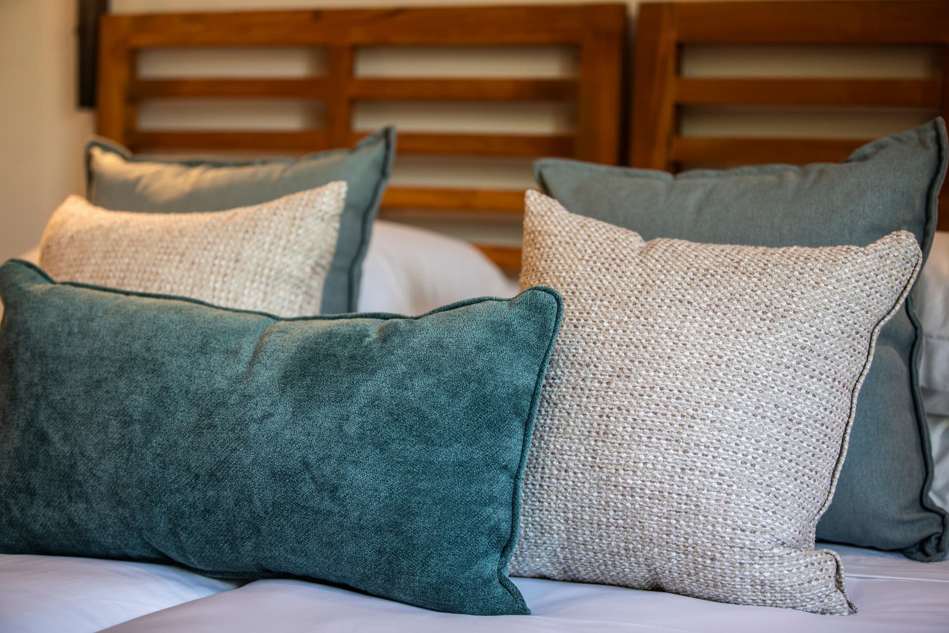 Tons doux et textures variées sur des coussins en lin et velours.  
Éléments en bois ajoutant chaleur au décor de la chambre.  
Couleurs apaisantes créant une ambiance sereine et relaxante.  
Agencement harmonieux des textiles offrant du confort visuel.  
Éclairage subtil mettant en valeur les détails du mobilier.