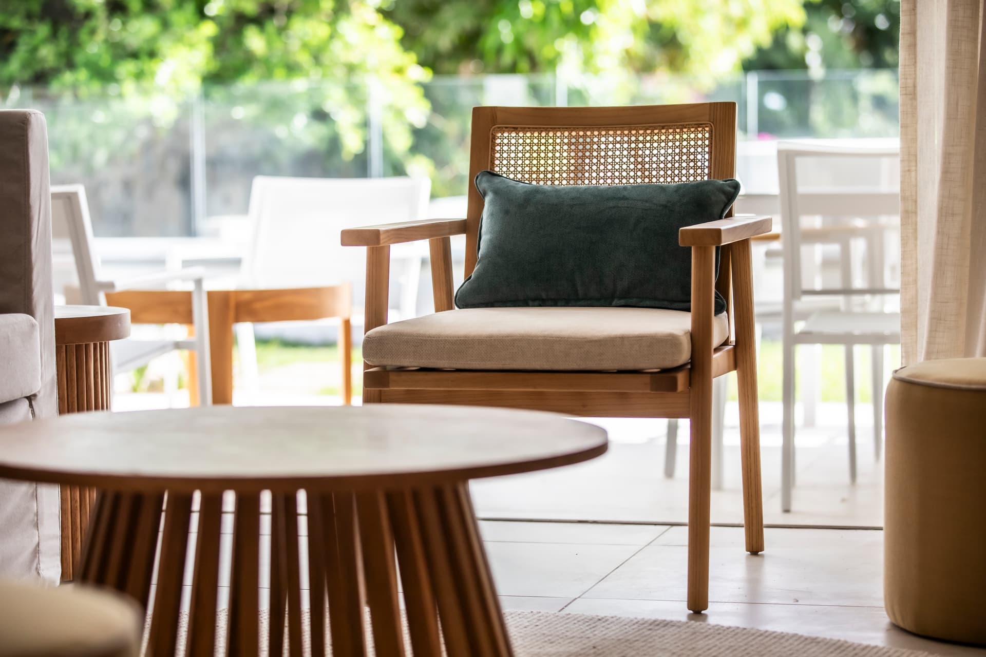 Chaise en bois avec coussin confortable dans un salon lumineux.  
Table basse arrondie en bois apportant une touche moderne.  
Espace de vie bien agencé avec vue sur l'extérieur.  
Éclairage naturel entrant par la baie vitrée, créant une ambiance aérée.  
Mobilier minimaliste offrant un cadre fonctionnel et agréable.
