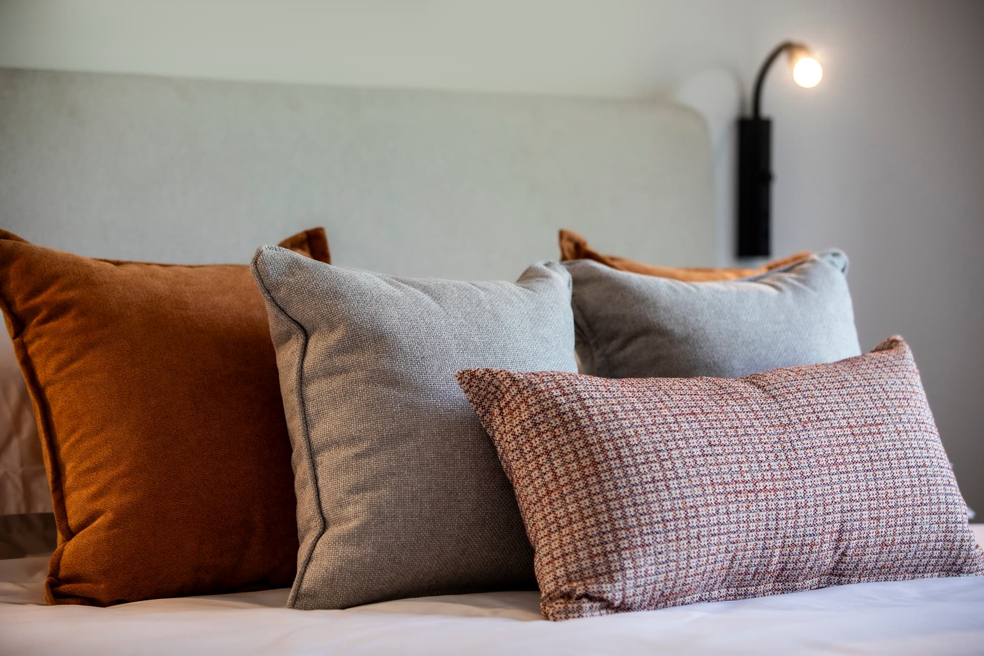 Coussins en velours et lin ajoutant une touche de confort au lit.  
Tête de lit en tissu clair avec un design épuré.  
Éclairage mural discret mettant en valeur le décor de la chambre.  
Ambiance chaleureuse grâce à une palette de couleurs douces.  
Agencement réfléchi favorisant une atmosphère reposante.