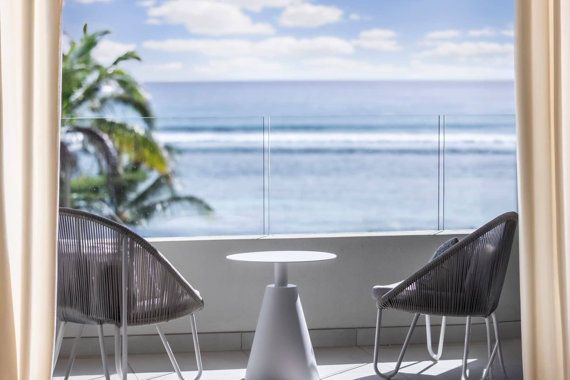 Vue dégagée sur l'océan depuis le balcon avec mobilier extérieur.  
Espace de détente offrant une ambiance tranquille et apaisante.  
Baies vitrées laissant entrer la lumière naturelle dans la pièce.  
Coussins confortables ajoutant du style aux chaises sur la terrasse.  
Décor minimaliste mettant en valeur le panorama environnant.