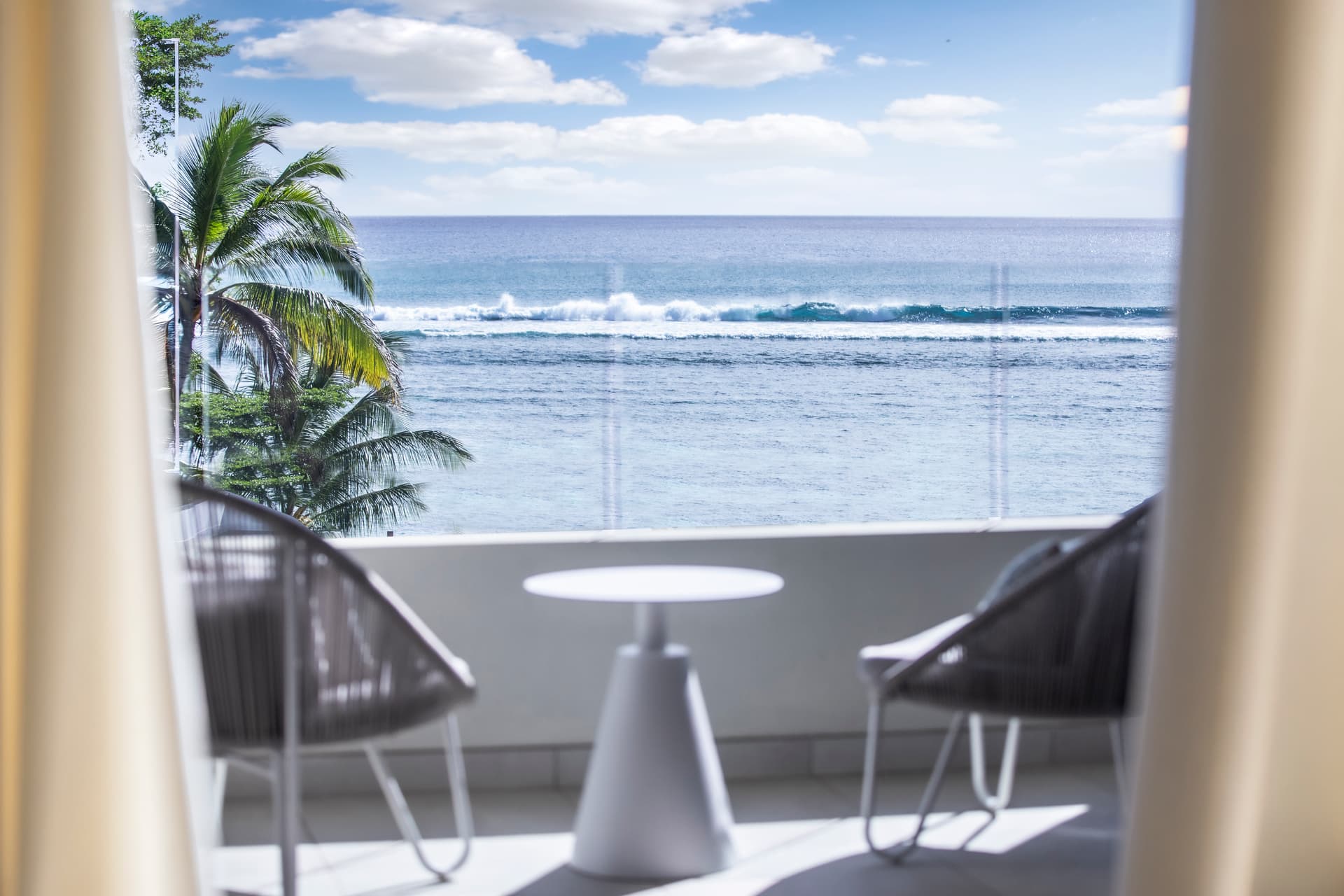 Vue sur l'océan depuis le balcon avec mobilier moderne.  
Espace extérieur offrant une atmosphère calme et relaxante.  
Coussins sur les chaises ajoutent du confort au coin détente.  
Baies vitrées maximisant la lumière naturelle dans la pièce.  
Décor épuré mettant en valeur le paysage maritime environnant.